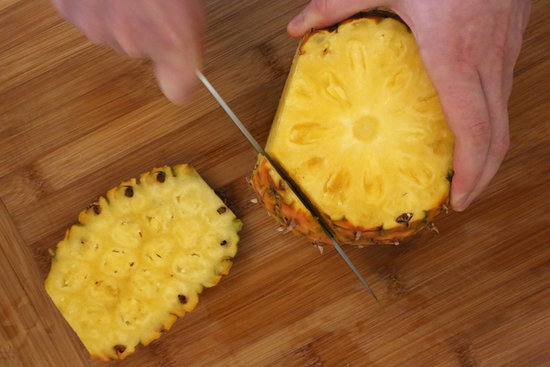 Run the knife down the length of the pineapple. You want to cut in deep enough so that all the prickly brown bits are cut off. I make about seven cuts, but you could do more or less, depending on how much you chop off, and how big your pineapple is.
Run the knife down the length of the pineapple. You want to cut in deep enough so that all the prickly brown bits are cut off. I make about seven cuts, but you could do more or less, depending on how much you chop off, and how big your pineapple is.